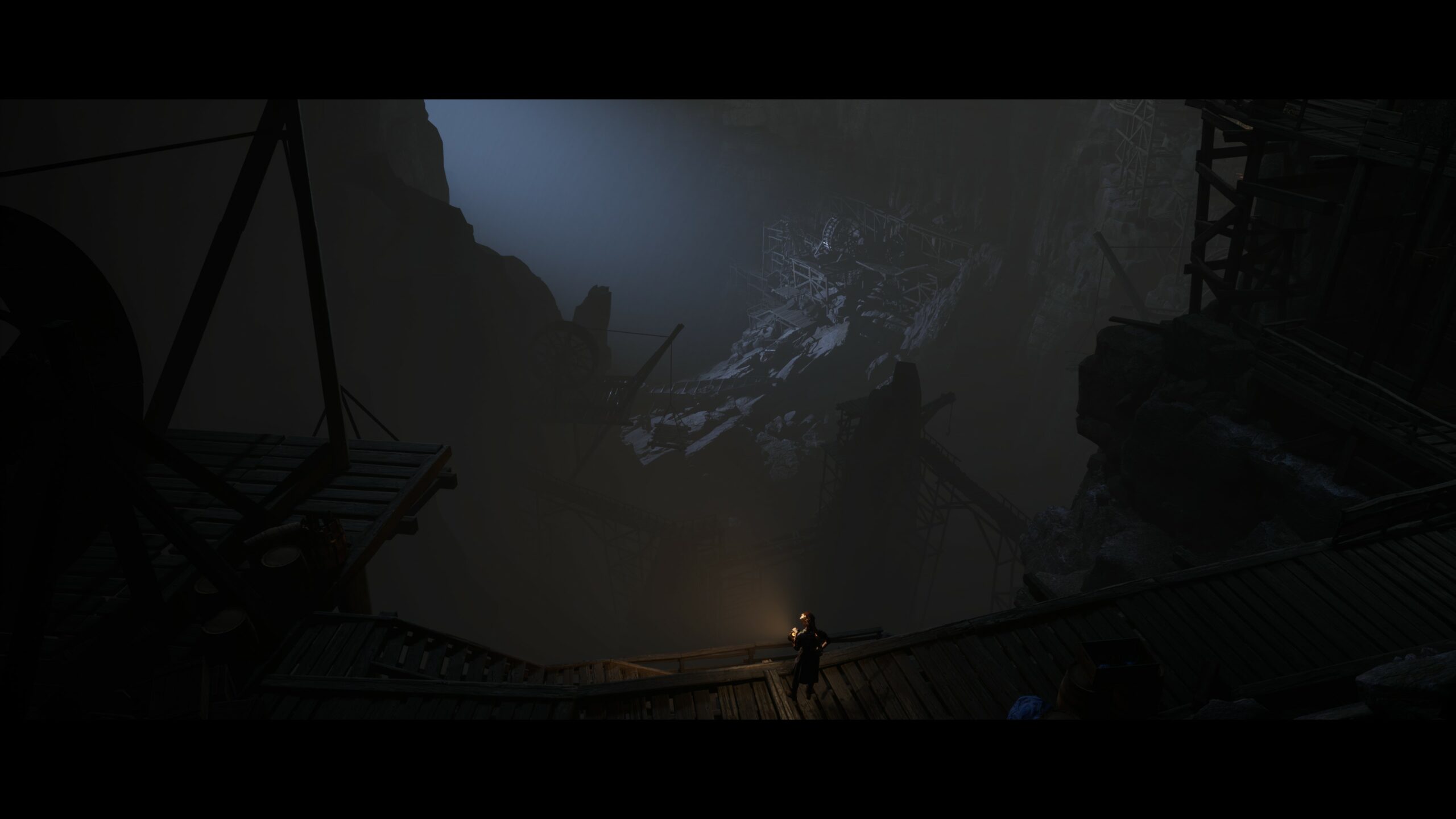 Captura de pantalla de Eriksholm: The Stolen Dream mostrando el acceso a las gigantescas minas, en primer plano sobre unas plataformas de madera la protagonista con una linterna y lejos abajo y al fondo, el resto de la mina iluminada por una tenue luz azulada.